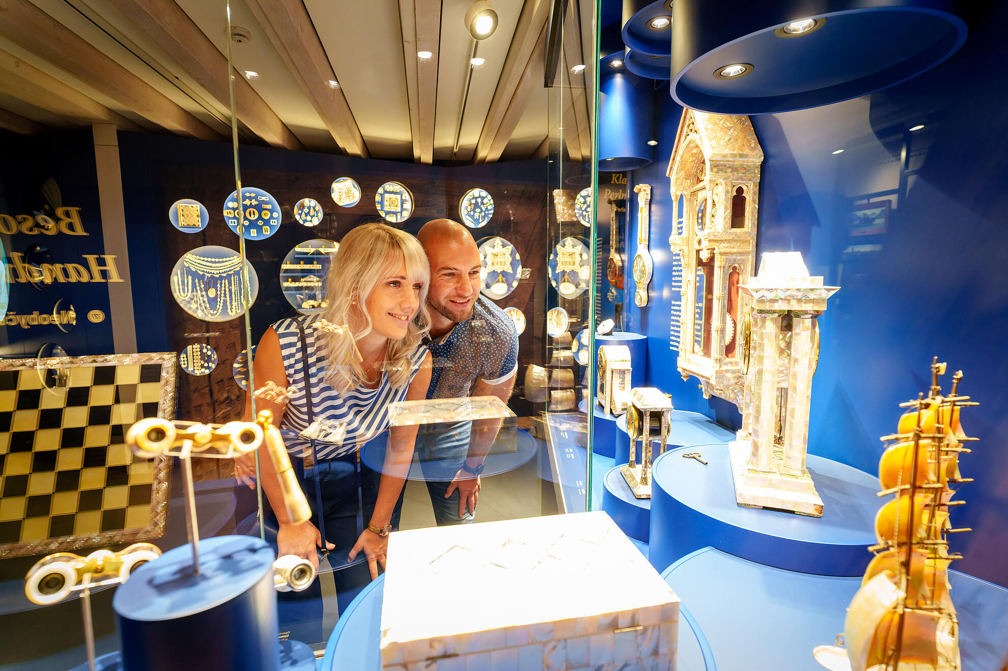 Ein Mann und eine Frau stehen im Erlebnismuseum Perlmutter vor einer beleuchteten Vitrine und betrachten die ausgestellten Objekte.